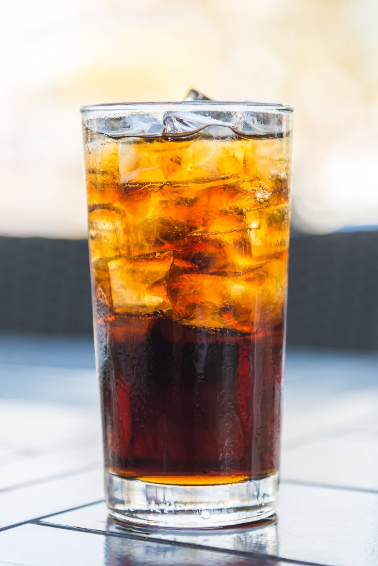 Erfrischendes Glas Cola mit Eiswürfeln, außen beschlagen, serviert auf einem hellen Fliesentisch im Außenbereich